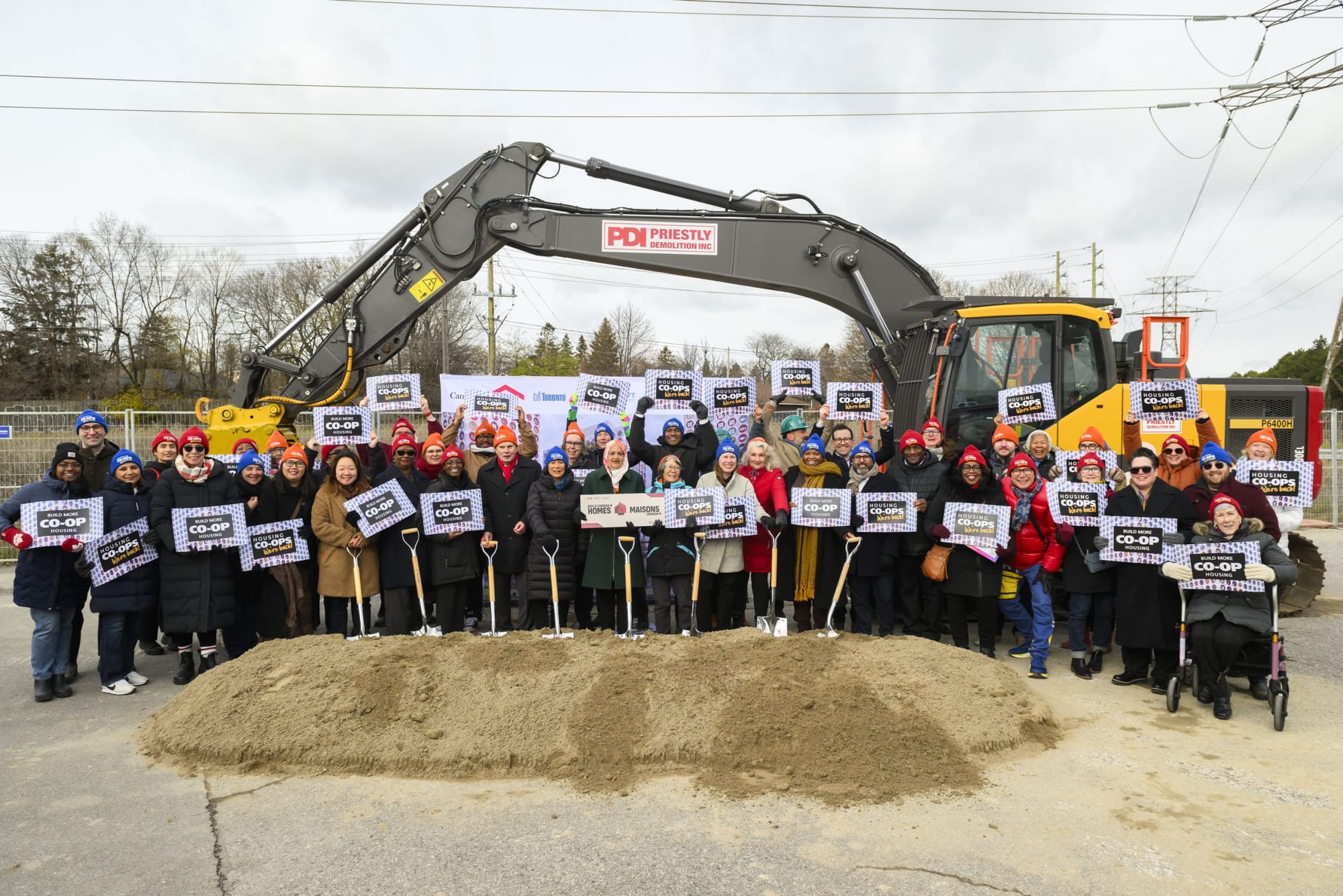 A large group of people holding co-op signs pose in front of a backhoe.