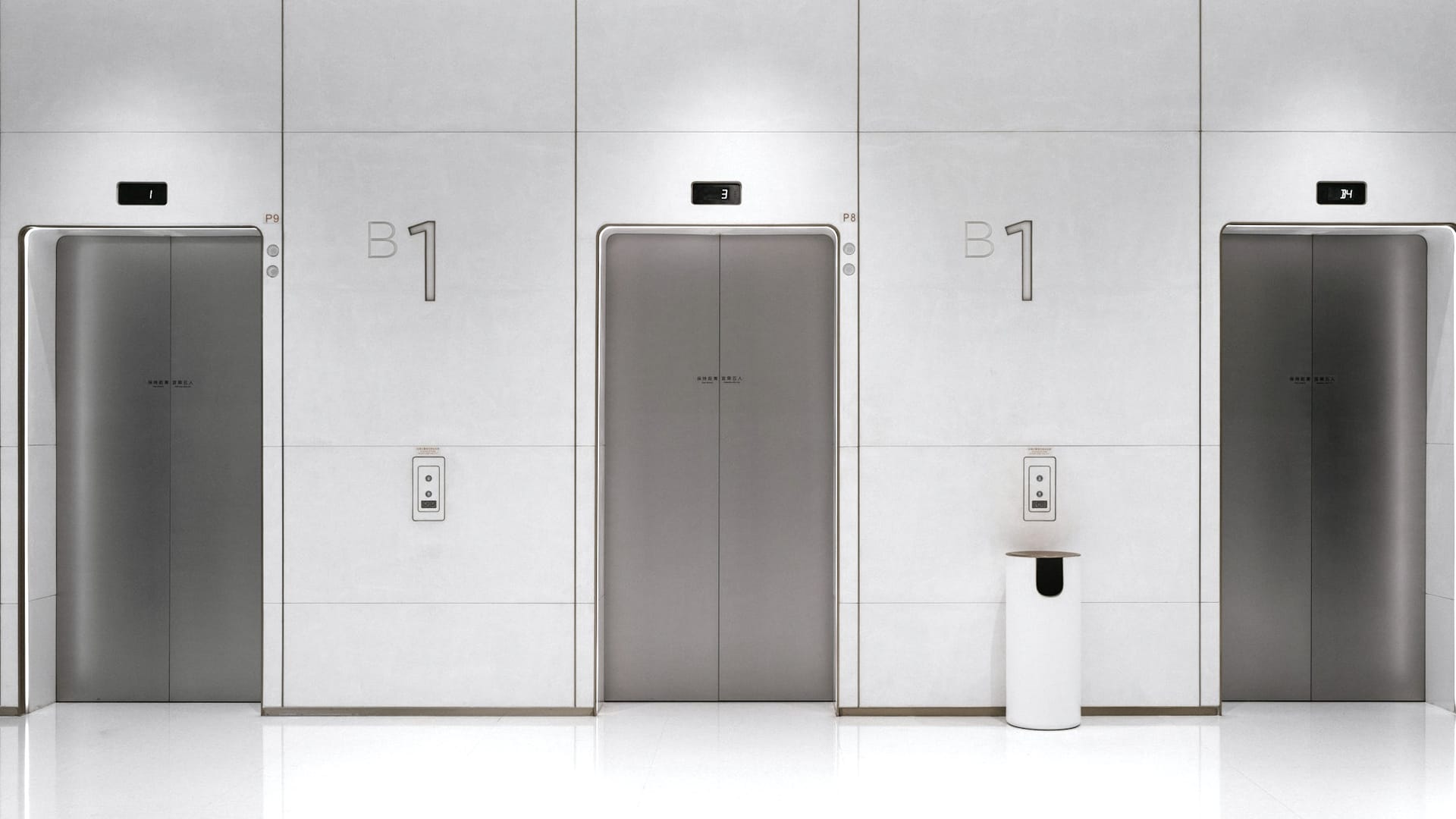 Three elevator doors in a white lobby.